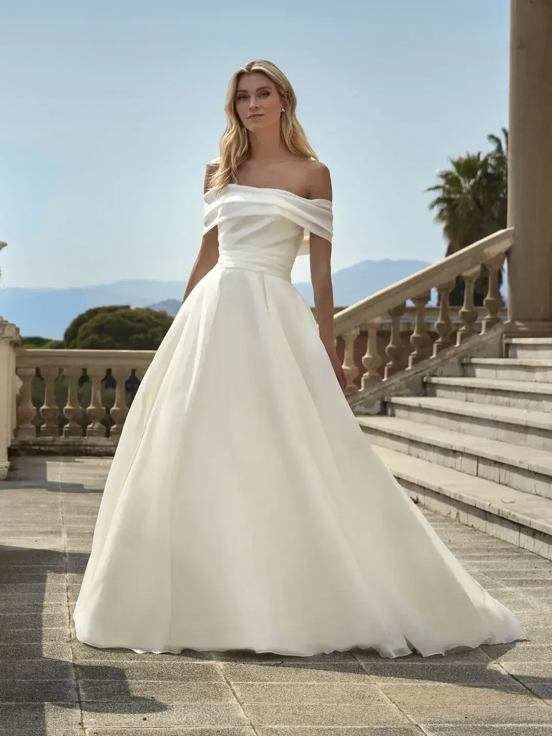 model is wearing an off the shoulder ball gown wedding dress