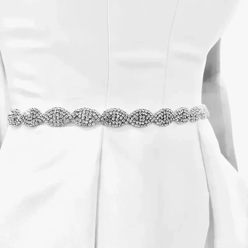A close-up of a sparkling silver belt with intricate patterns, worn over a white dress.