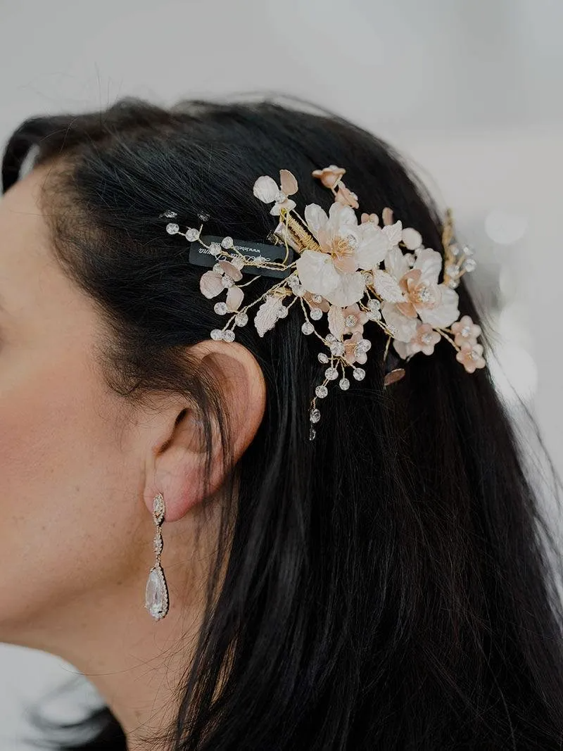 A close-up of a woman's hair, adorned with a decorative hairpiece featuring flowers and pearls, alongside an elegant earring.