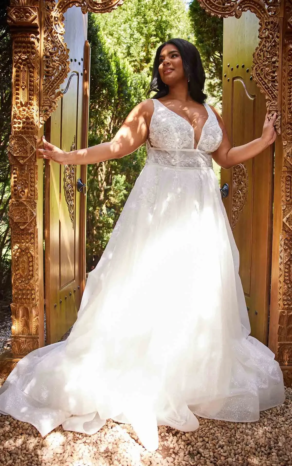 Model wearing a plus-size ivory A-line wedding gown with a deep V-neckline, lace bodice, defined waist, and flowing skirt.