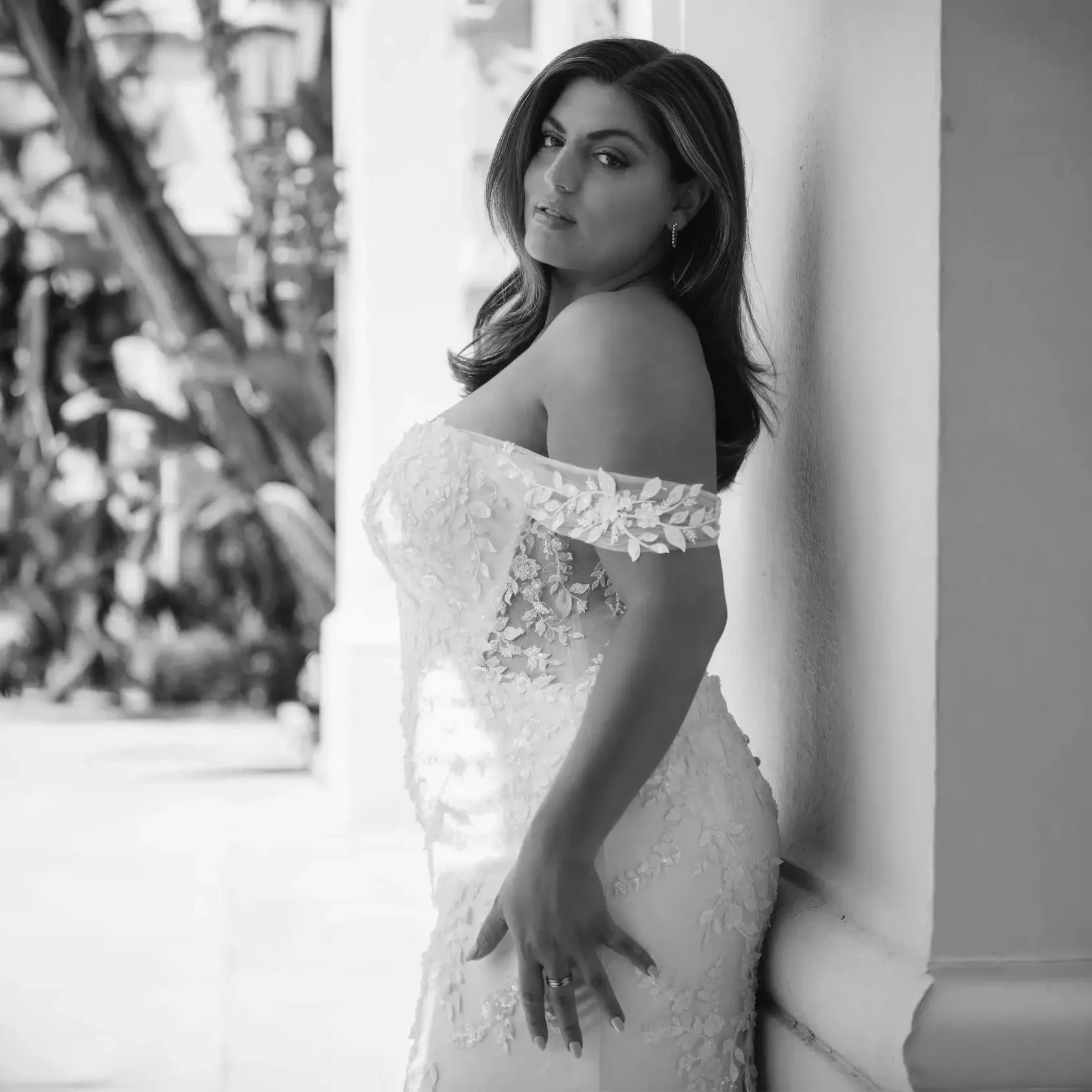 Plus-size bride wearing an off-the-shoulder fitted lace wedding gown with floral appliqués and sheer side detailing.